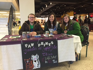 In the picture of the booth from left to right are Matthew Graham, Emily Hercules, and Amanda Lutz. Photos are of the booth, volunteers working the booth, and pictures from Paw Prints